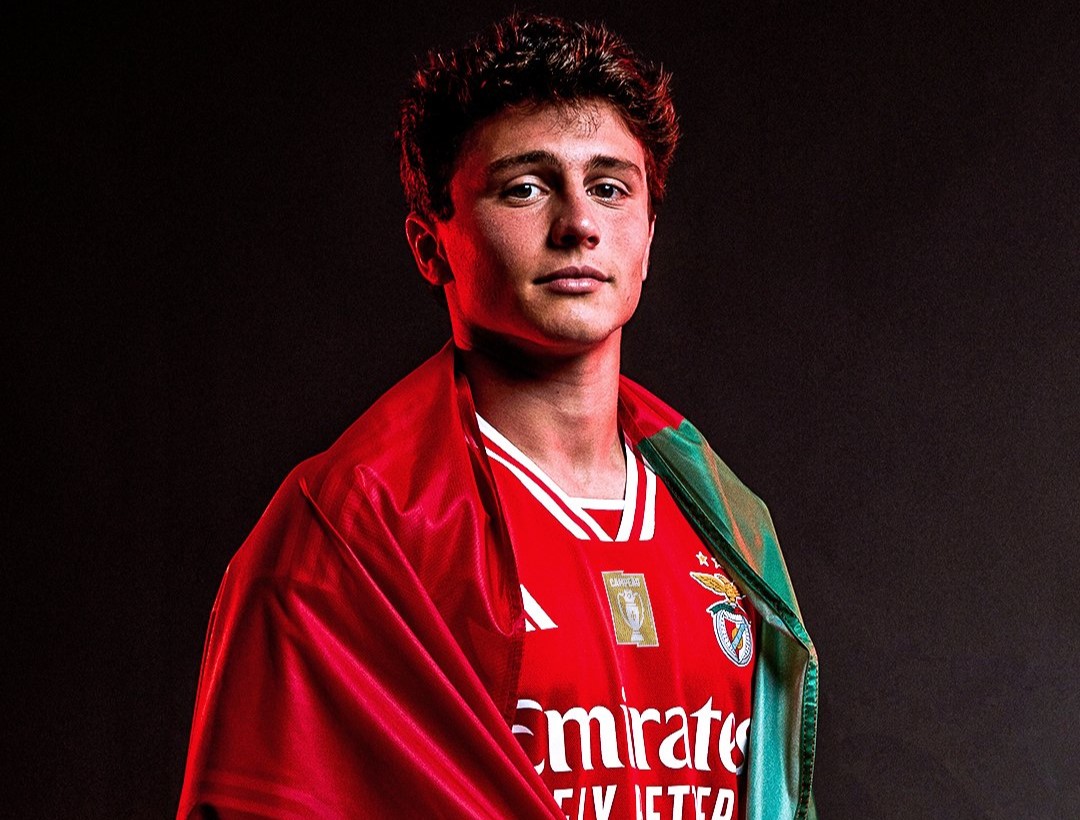  A young Portuguese footballer, Joao Neves, who plays for Benfica, is pictured here wearing a red jersey and a green and red scarf with the Benfica logo on it.